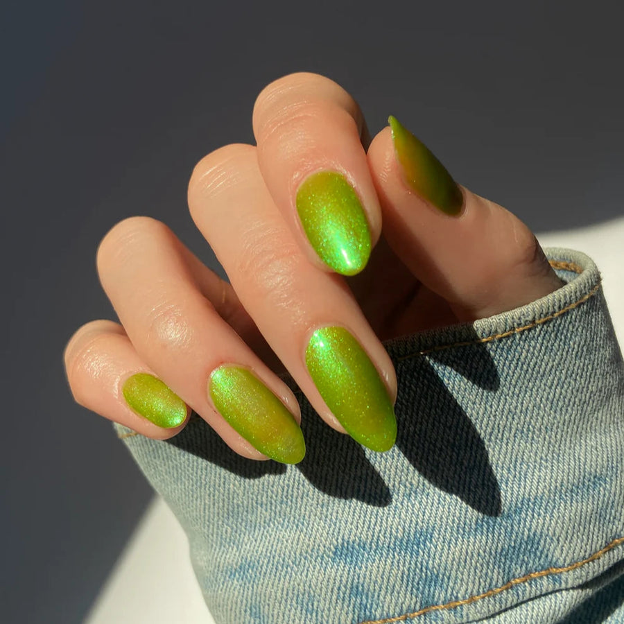 Hand with green nail polish wearing a denim sleeve against a dark background